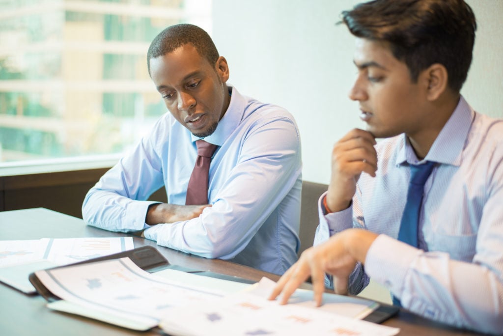 telstra. image shows two men looking at graphs, charts and spreadsheets.