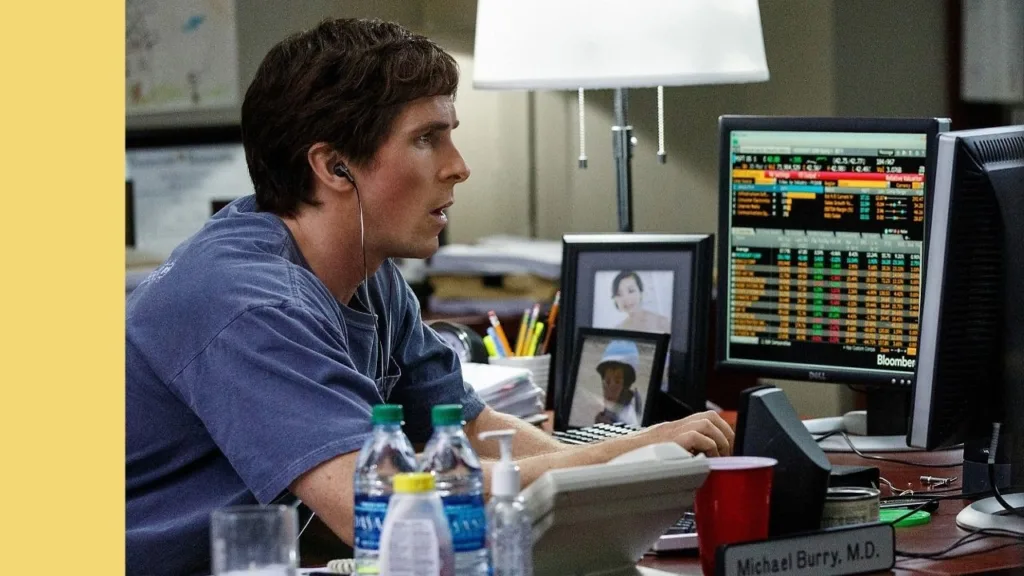 Actor Christian Bale potraying investor Michael Burry intensely looks at a computer screen showing stock market data