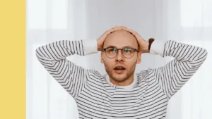 Man has hands on his head and an expression of shock on his face