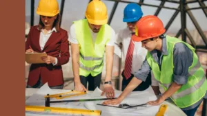 Construction workers in high vis and hard hats look over plans on a table