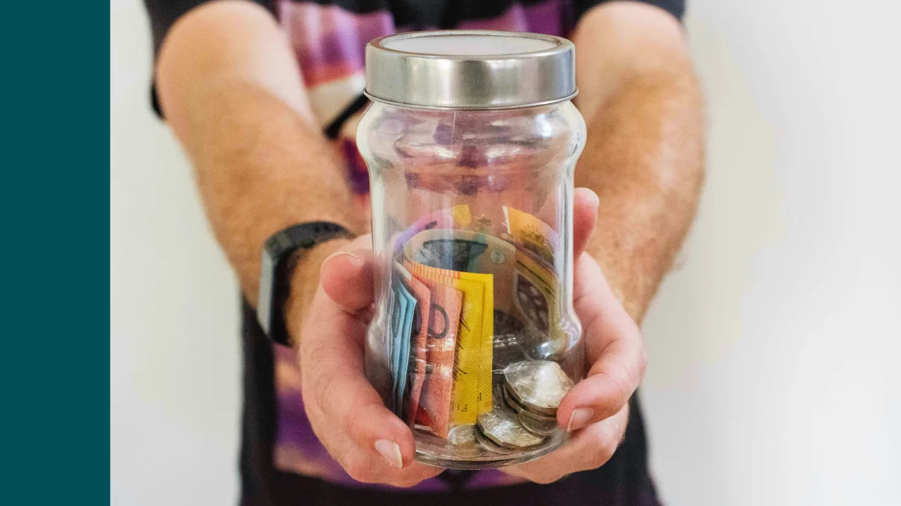 Person holding a glass jar with cash and coins